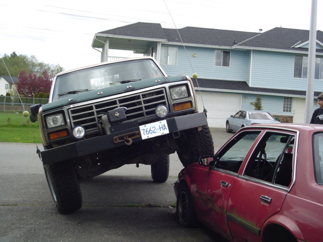 Lifted green Ford pickup crushing a red sedan in a driveway, BC plate 7662 HA