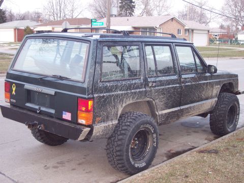 1993 Jeep Cherokee - This muddy Jeep Cherokee is parked on a residential street, showing its aftermarket bumper and off-road tires.