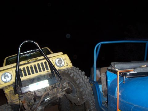 1991 Ford Bronco - Two off-road vehicles are seen at night, one yellow and one blue, with the yellow vehicle angled forward.