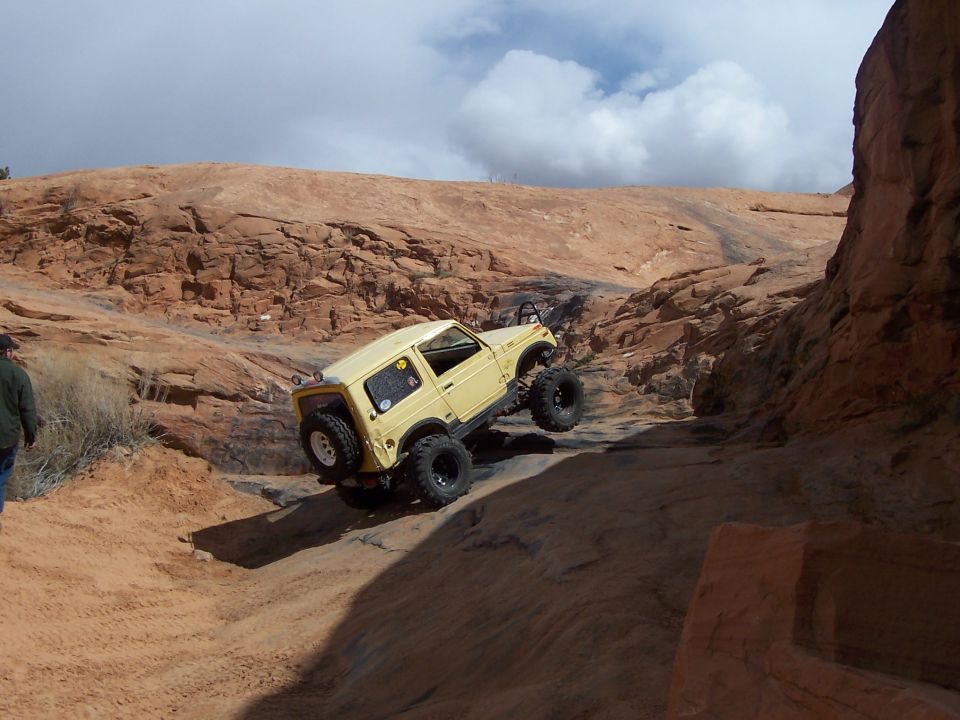 yellow off-road SUV climbing a steep, rocky incline with a person walking nearby
