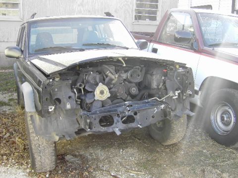 1998 Jeep Cherokee - Front view of a 1998 Jeep Cherokee showing engine and damage, with another vehicle nearby.