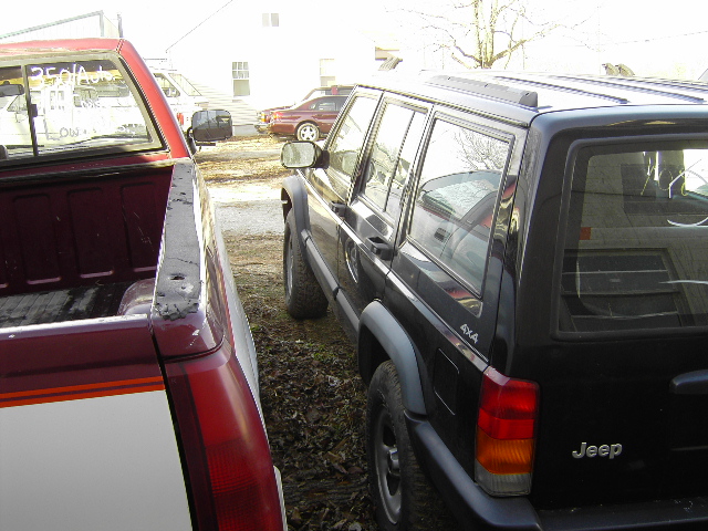 Black Jeep Cherokee, rear quarter view, parked next to a red and white pickup truck