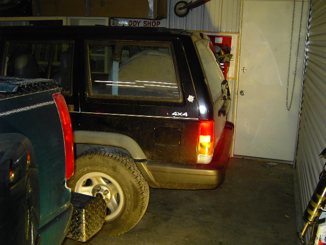 Rear view of black 1998 Jeep Cherokee with 4x4 badge parked next to a dark pickup truck