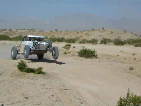 White off-road race buggy jumping over a desert berm with mountains behind