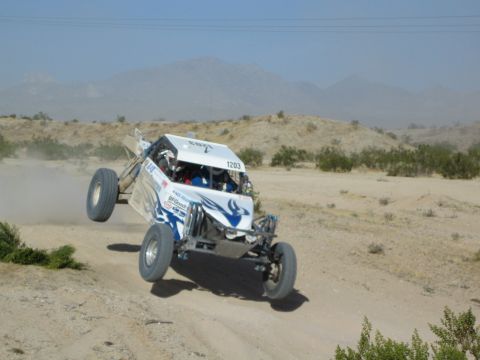White and blue off-road buggy number 1203 launching off a desert jump