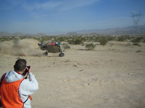Photographer in orange vest filming an off-road buggy crashing in the desert
