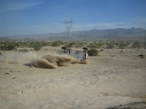 Off-road buggy on its side raising dust beneath a transmission tower in desert