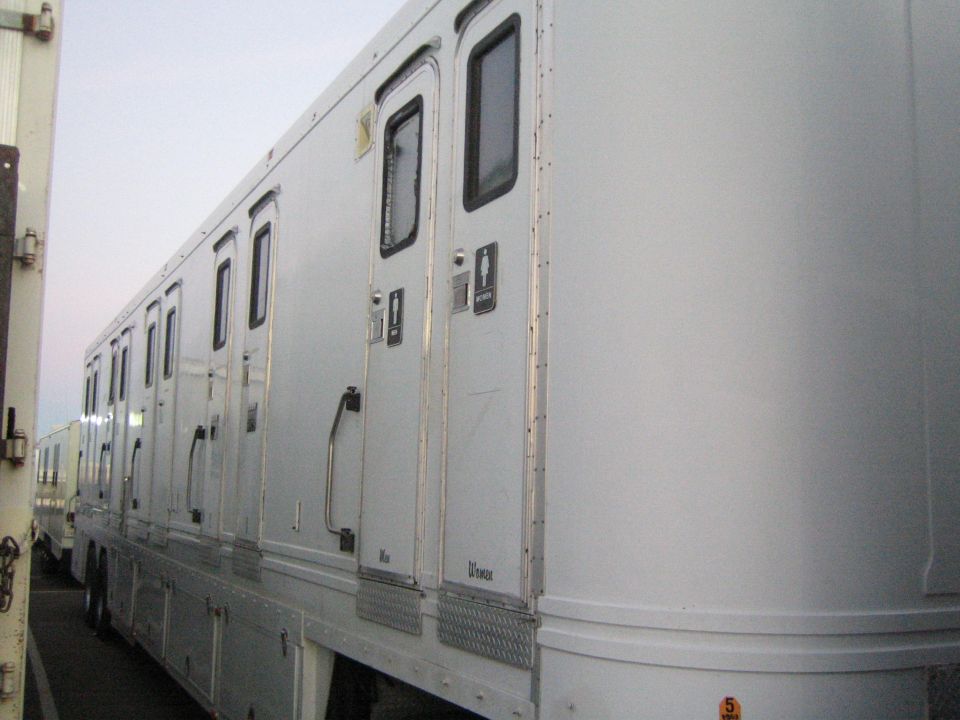 Row of white portable restrooms with multiple doors and windows, parked outdoors