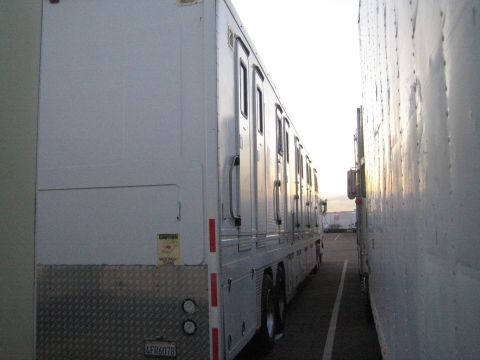 1968 Ford Mustang - A long white trailer with numerous doors is parked tightly between two other large vehicles.