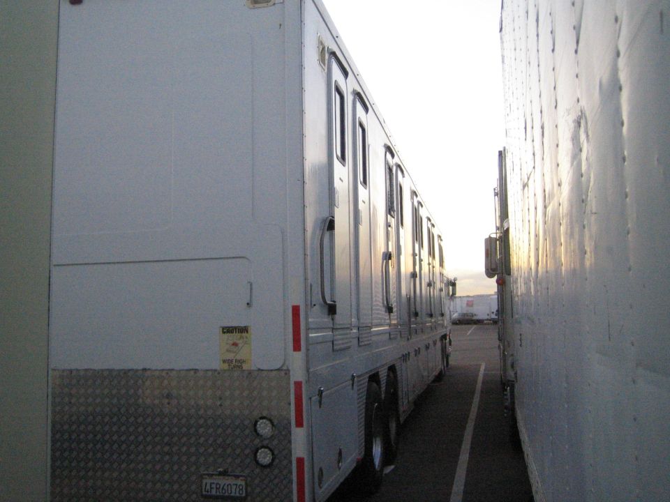 Side view of a white trailer with multiple doors parked between two trucks