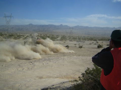Spectator in orange vest watches a dust cloud from an off-road racer in desert