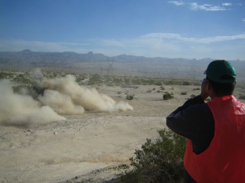 Spectator in orange vest watching dust cloud from off-road racer in desert