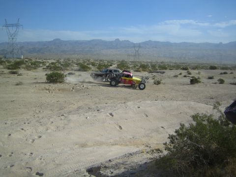 Red-yellow off-road buggy passing a dark sedan racer in the desert