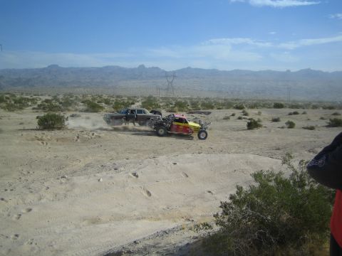 Red-yellow buggy and dark sedan racing side by side in the desert