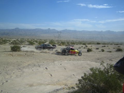 Dark sedan racer leading a red-yellow buggy across the desert