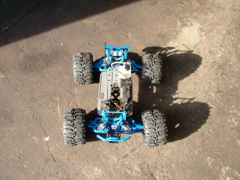 1994 Ford Bronco - A blue remote control monster truck chassis with exposed wiring sits on a cracked concrete surface.