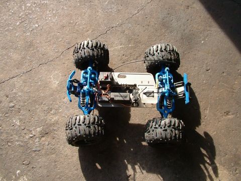 1994 Ford Bronco - The underside of a blue remote control monster truck chassis is shown, revealing its suspension and electronic components.
