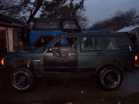 1993 Jeep Cherokee - A dark green 1993 Jeep Cherokee is parked next to a blue Jeep, with a house and trees visible.