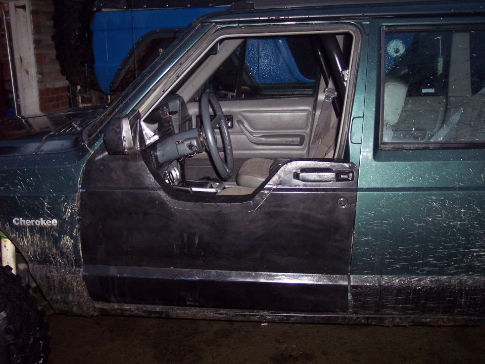 1993 Jeep Cherokee interior showing dashboard, steering wheel, and open driver's door. Another vehicle is visible behind it