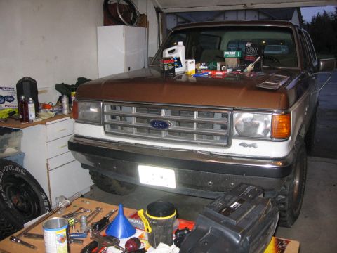 1987 Ford Bronco - A 1987 Ford Bronco sits in a garage, its hood covered with various automotive parts and tools.