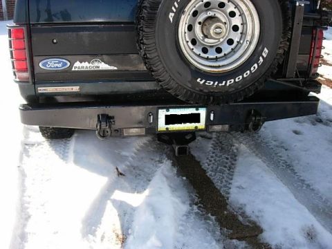 1993 Ford Bronco - The rear of a dark green Ford Bronco is shown with a spare tire and a heavy-duty aftermarket bumper in the snow.