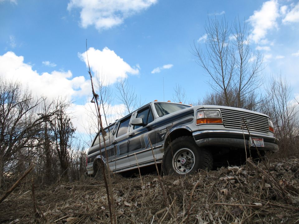 Lifted white four-door Ford Bronco conversion tilted on a brushy dirt bank