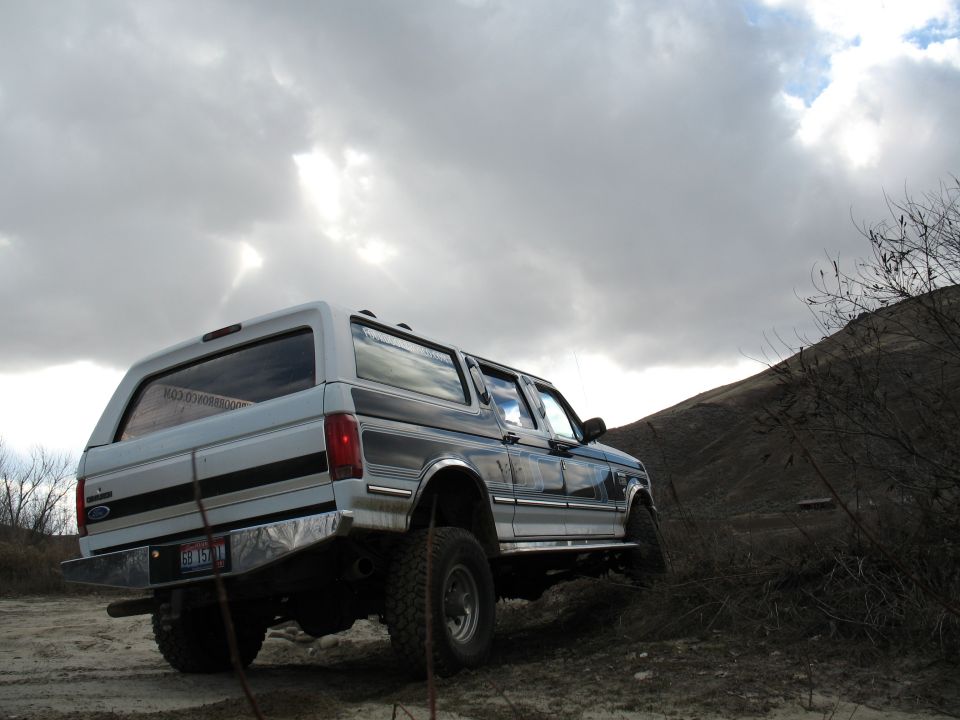 Lifted white four-door Ford Bronco conversion flexing on a dirt bank under storm clouds