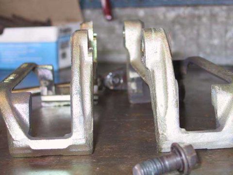 1997 Ford Taurus - Close-up of two brake caliper brackets and a bolt on a workbench surface.