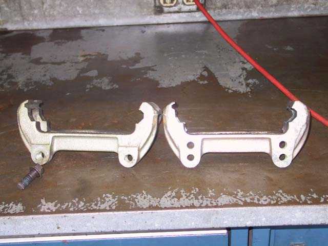 Two metal brake caliper spreaders and a bolt on a workbench