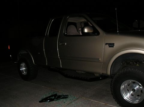 1999 Ford F-150 - A gold pickup truck is parked on a paved surface at night, with broken glass on the ground in front of it.