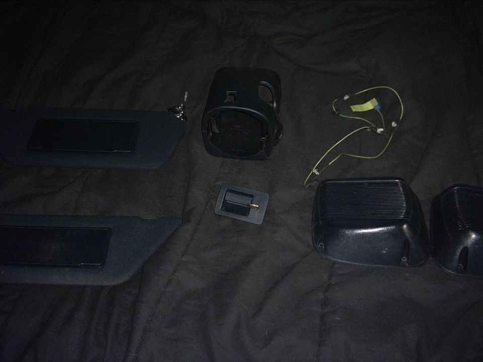 Two sun visors, a speaker housing, a door handle, and two side mirror housings laid out on a dark surface