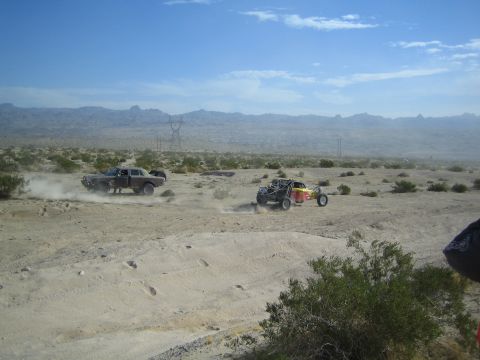 Dark sedan and red-yellow buggy racing in the open hazy desert