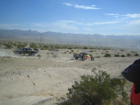 Dark sedan and red-yellow buggy racing across hazy desert terrain