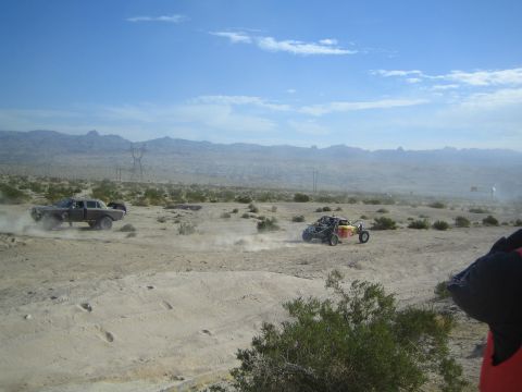 Dark sedan leading a red-yellow off-road buggy across desert flats