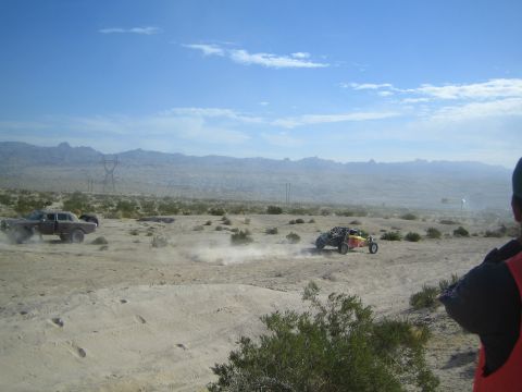 Dark sedan and red-yellow buggy racing into the distance across the desert