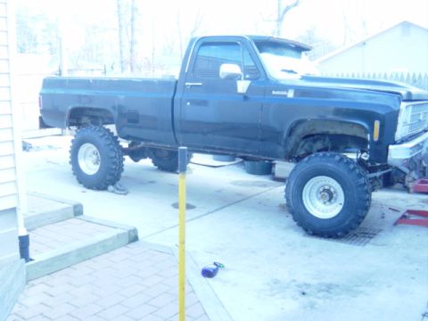 1987 Suzuki Samurai - A lifted pickup truck with oversized tires sits parked in a driveway, appearing to be undergoing modifications.