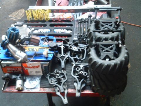 1994 Ford Bronco - Various parts for an RC car, including an engine, suspension components, and large tires, are organized on a workbench.