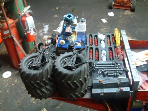 1994 Ford Bronco - A collection of remote-controlled car parts, including large tires, shock absorbers, and engine components, laid out on a workbench.