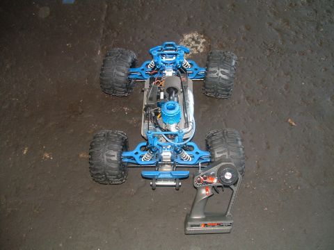 1994 Ford Bronco - A blue remote control monster truck with its engine exposed sits on a dark, textured surface next to its controller.