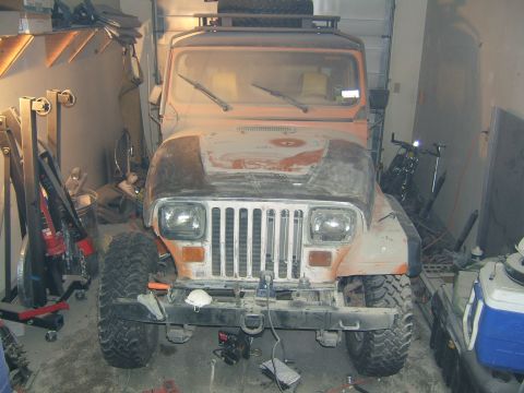 1989 Jeep YJ - This Jeep Wrangler is parked indoors, surrounded by tools and equipment, with a spare tire on the roof rack.