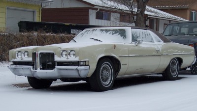 1972 Ford Ranchero - This 1971 Pontiac Grandville coupe is partially covered in snow, with a dark-colored vehicle visible behind it.