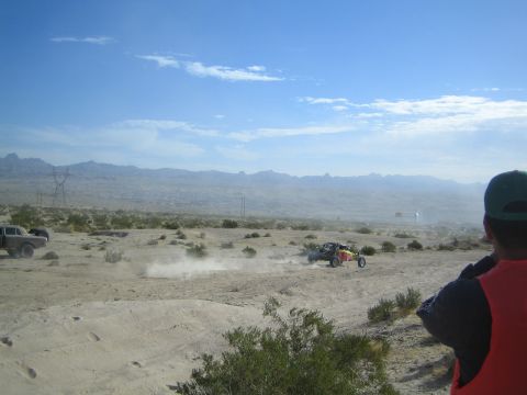 Spectator in orange vest watching an off-road racer cross distant desert