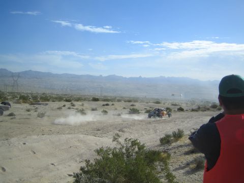 Spectator in orange vest watching off-road racer in distant hazy desert