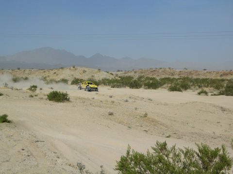 Yellow off-road buggy driving on a sandy desert trail with mountains behind