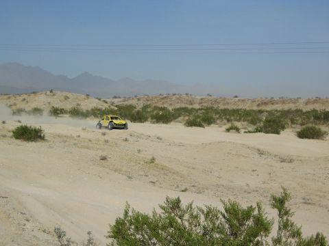 Yellow off-road buggy racing across open desert with distant mountains