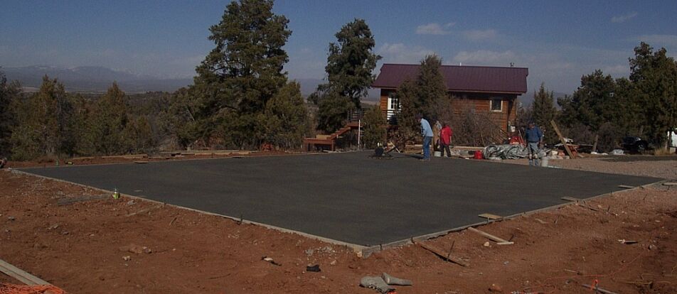 Freshly poured concrete slab at a hilltop building site with cabin and mountains