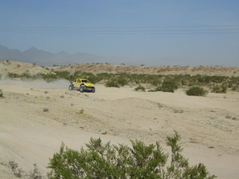 Yellow desert race buggy speeding past scrub brush in arid terrain