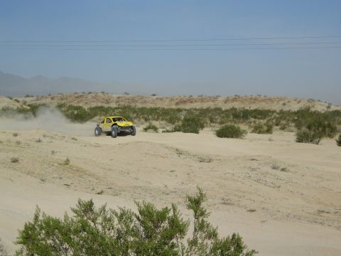 Yellow off-road race buggy on desert course with mountains behind