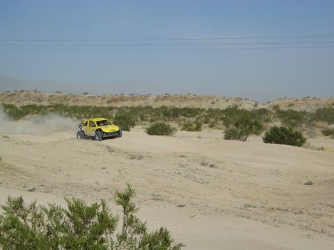 Yellow off-road buggy cresting a sand berm in the desert