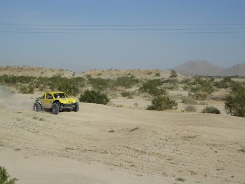 Yellow off-road race truck racing across sandy desert toward mountains